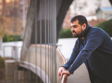 Olgun sakallı adam gün batımında Madrid Köprüsü 'nün korkuluklarına yaslanıyor..