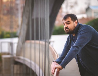 Olgun sakallı adam gün batımında Madrid Köprüsü 'nün korkuluklarına yaslanıyor..