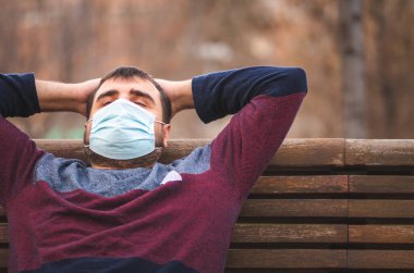 Koruyucu maskeli adam gün batımında bankta oturmuş dinleniyor.. 