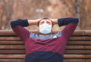 Koruyucu maskeli adam gün batımında bankta oturmuş dinleniyor.. 