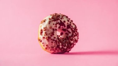 Beyaz çikolatalı donut ve pembe arka planda dönen bademler..