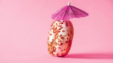 Badem soslu beyaz çikolatalı çörek ve pembe arka planda dönen dekorasyon şemsiyesi..