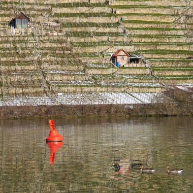 Nehirde kırmızı şamandıra var. Arka planda da barakalar var. Kış.