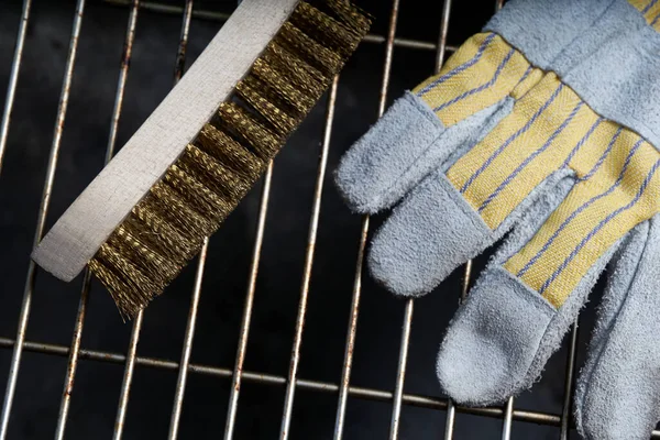 Kirli ızgara pasının üzerinde duran tel fırça ve koruyucu eldiven. Üst görünüm.