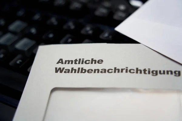 Black letters on white envelope saying: Official election notification (german: Amtliche Wahlbenachrichtigung). Black keyboard in background. depth of field. 2021 federal election in germany. Closeup.