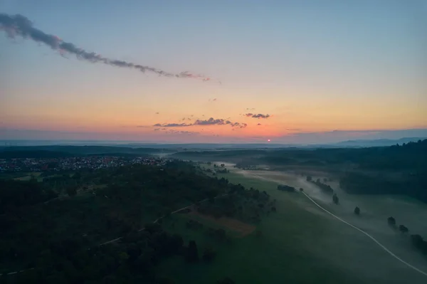 Small village in germany. fog lies in the valley near the forest. sun rises on the horizon. Copy space in the sky. Germany, Reudern.