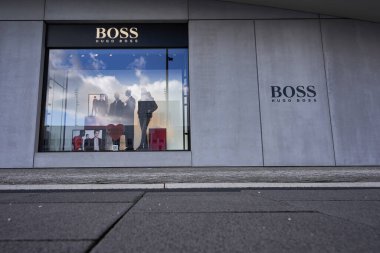 Metzingen, Almanya - 20 Mart 2021 Hugo Boss Outlet mağazası. Siyah cepheli vitrin mankeni olan vitrinler. Ön planda kaldırım taşları var. Ön manzara. geniş açı.