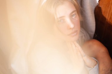 Gri keten gömlekle makyajsız genç güzel bir kadının ahşap iç mekânında güneş ışığıyla portresi.