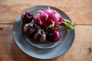 Mor erikler, mangosenler, ejderha meyvesi ve bıçak. Tahta masadaki seramik tabakta.