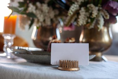 Çatal ve bıçaklı seramik tabaklarda çikolatalı kekler, tekstil peçetesi, beyaz isim kartı ve ahşap masadaki çiçekler.