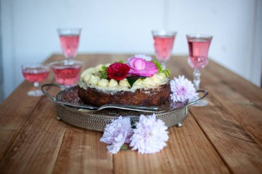 Kutlama pastası ve kadehte gül şarabı, doğum günü için tahta masada çiçekler.