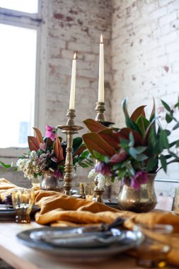 Süslü süslemeleri olan uzun ahşap bir masa, şamdanlar, vazolar, tabaklar ve yemekler beyaz tuğlalı bir odada.
