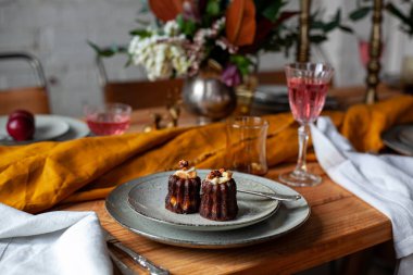 Şık dekorasyonlu uzun ahşap masa, şamdanlar, çiçek vazoları, şaraplı bardaklar, tabaklar ve beyaz tuğlalı duvarlı bir odada yemek.