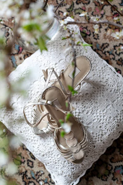 sandals of the bride on a white lace pillow on the carpet through a flowering branch of a cherry tree
