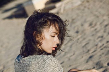 Büyük dudakları ve kumsalda kapalı gözleri olan güzel esmer kadın portresi.