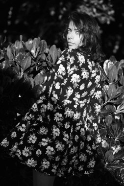 Güneşli bir günde çiçek desenli giyinmiş güzel, gülümseyen esmer bir kadının siyah beyaz portresi.