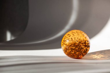 İçinde hava kabarcıkları olan turuncu cam top beyaz-gri arka planda güneş ışığıyla aydınlatılıyor.