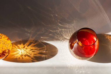 Gri arka planda kırmızı cam bardakta mum ve baloncuklu turuncu cam top.