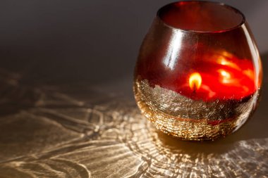 Kırmızı cam bardaktaki mum gri arka plan ışığı ve gölge desenleri