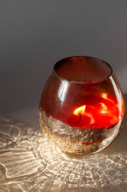 Kırmızı cam bardaktaki mum gri arka plan ışığı ve gölge desenleri