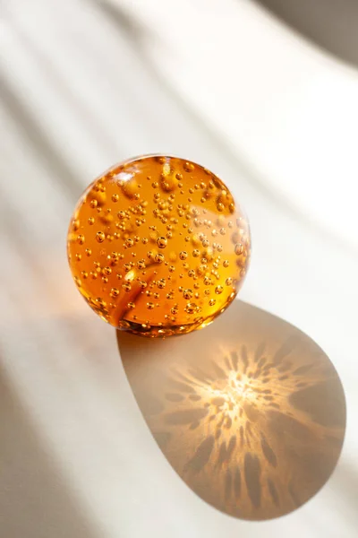 Boule de verre orange avec bulles d'air à l'intérieur éclairées par la lumière du soleil sur un fond blanc-gris Images De Stock Libres De Droits