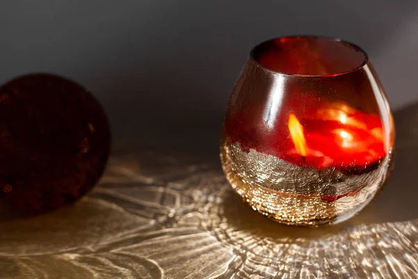 Bougie dans une tasse en verre rouge sur un fond gris motifs de lumière et d'ombre Photo De Stock