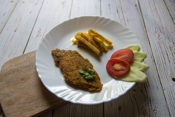 Close up of Bengali delicacy fish fry along with french fries and salad in a plate on a wooden platter.