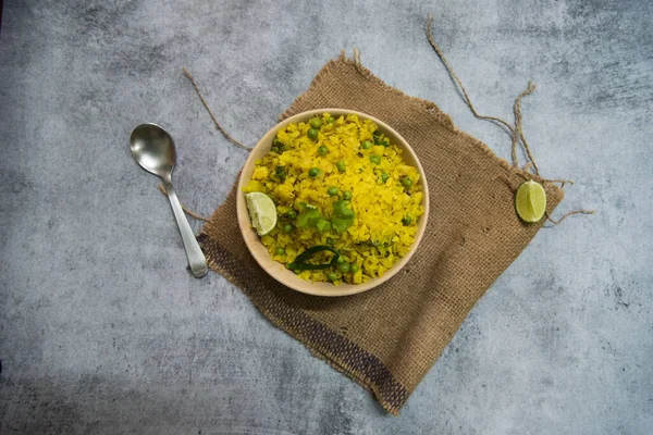 Breakfast food item poha with coriander and lemon in a bowl.