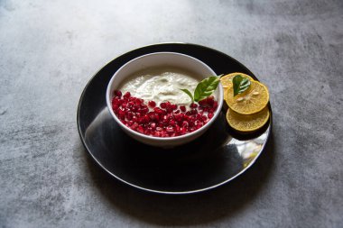 Nar tohumları ve siyah bir tabakta taze yoğurt.