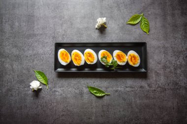 Kaynamış yumurta dilimlerinin üst görüntüsü siyah bir tabakta seçici bir odaklanma ile sıralanmış..