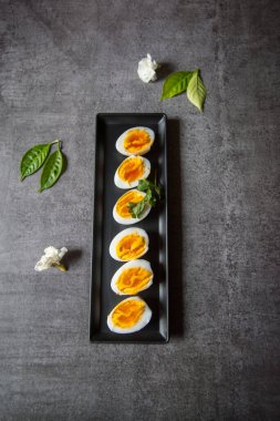 Kaynamış yumurta dilimlerinin en üst görünümü koyu bir arka planda bir tepside.