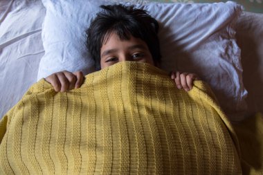 Yatakta tembelce uyanan ve seçici bir odak noktasıyla uyanan bir çocuk. Yatakta tembel bir pazar günü kavramı.