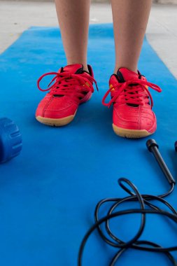 Sports and recreation background with legs of a boy, dumb bells and skipping rope in the outdoors. Close up, selective focus.