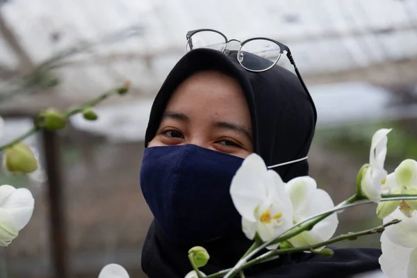 Beautiful female tourists who wear hijab visiting flower gardens during the pandemic wear masks to comply with health and safety protocols from COVID-19 : Yogyakarta, Indonesia : June 3, 2020