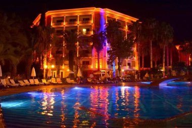 Akşamları havuz ve otel. İnsanlar akşam havuz başında dinlenir. Akşam otelinin ışıkları geceleri havuz suyuna yansıyor.. 