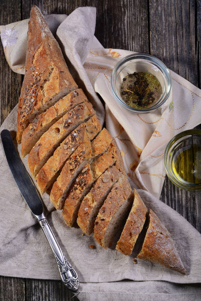 Свежий багет, разрезанный на куски, лежит на льняной салфетке на старом деревянном столе