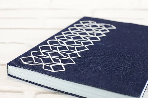 Handmade blue notebook with embroidered cloth cover with hexagons and white thread on brick background