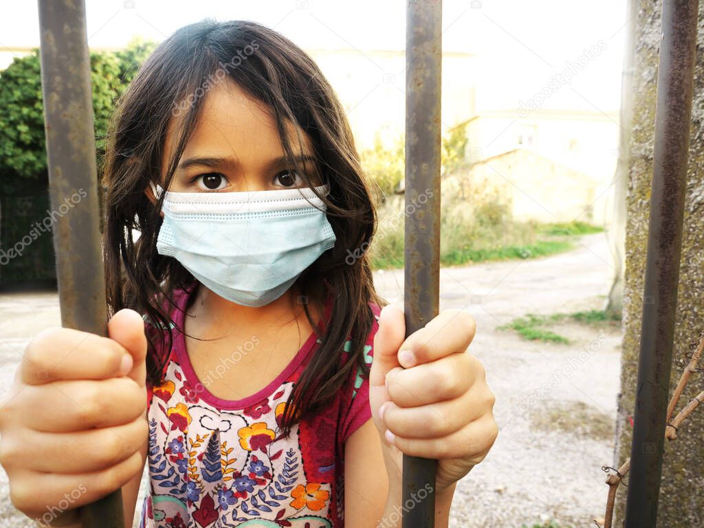 Photo of a little girl wearing a mask and holding bars