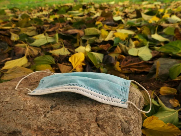 Máscara lançada na natureza em uma rocha no meio de folhas de outono — Fotografia de Stock