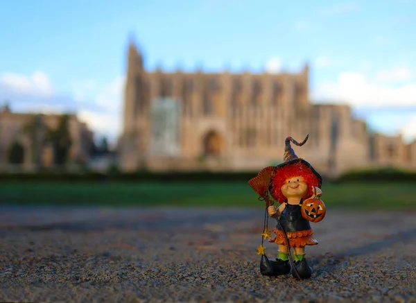 Süpürgeyle şapkalı, kızıl saçlı neşeli bir cadı ve ellerinde bir balkabağı, antik bir kalenin arka planında.