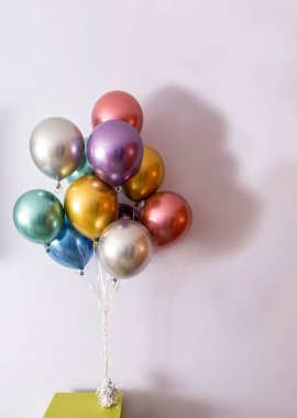 Metalik renkli helyum balonları bir yayla bağlanmış ve yeşil bir masada ağırlıkla tutuluyor, dikey format ve sağ tarafta kopyalama alanı.