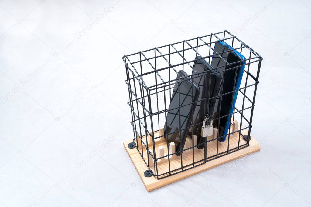 three cell phones locked in a cage with a padlock, concept of social isolation or phone abuse and social networks, white horizontal background