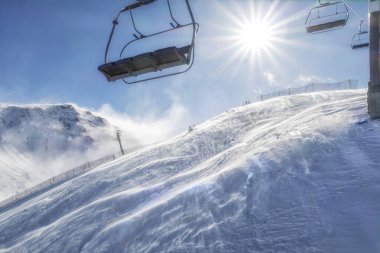 Güneşli bir günde, arka planda güneş ve yerde kar fırtınası esintisi olan bir kayak merkezinden başkanlık.