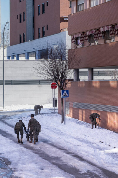 Army soldiers clean the streets of snow with shovels and spread salt to avoid freezing after the Filomena snowstorm, vertical