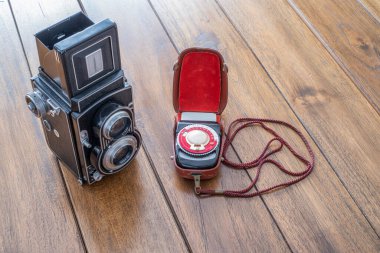 Tahta bir masanın üzerindeki antika ikiz mercek refleks kamerası ve antika bir el kamerası, yatay fotometre.