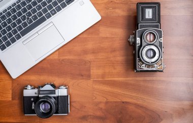 Eski bir 35 mm refleks kamera, ve eski bir orta format çift lens refleks kamera, onların yanında modern bir dizüstü bilgisayar, yatay