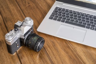 Modern bir dizüstü bilgisayarın yanındaki ahşap bir masada eski bir 35 mm refleks kamera, modern ve eski, horinzontal
