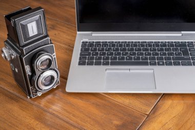 Modern ve antika bir çift lensli fotoğraf makinesinin yanında modern bir dizüstü bilgisayar.