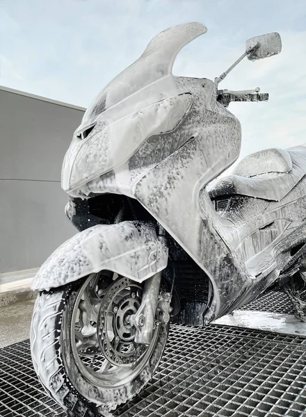 fully covered scooter with foam in a car wash, washing the scooter in a car and motorcycle wash store, close-up, vertical