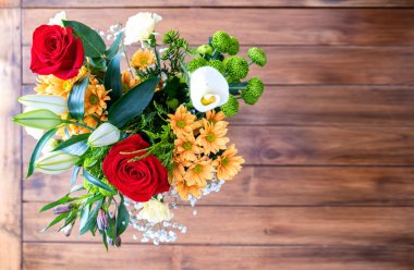 Üzerinde güller, zambaklar, papatyalar ve karanfiller olan bir buket çiçeğin üst görüntüsü, odağından çıkmış ahşap bir masa üzerinde, bukete seçici bir odak, yatay kopyalama alanı